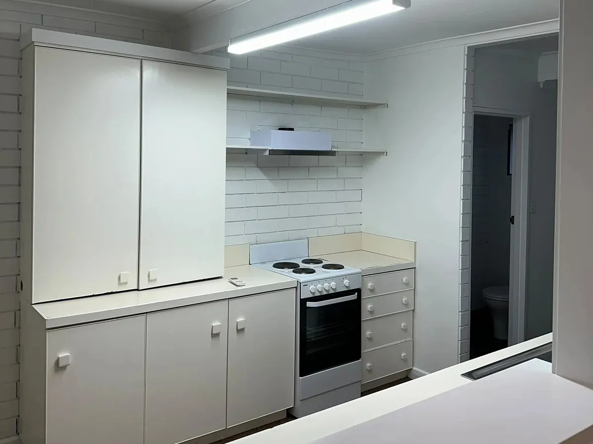 Empty kitchen with white cabinets, a white brick splashback and a freestanding electric stove